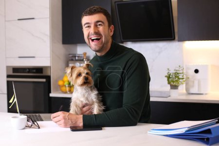 Téléchargez les photos : Portrait de beau jeune homme avec son petit chien mignon à la cuisine - en image libre de droit