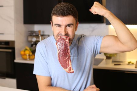 Photo for Portrait of handsome young man holding raw meat steak at kitchen - Royalty Free Image