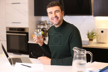 Foto de Retrato de un joven guapo bebiendo agua mientras trabaja desde casa en la cocina - Imagen libre de derechos