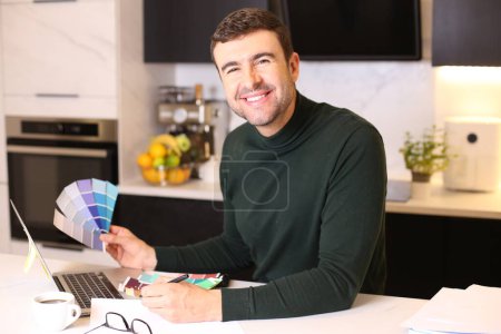Photo for Portrait of handsome young man with laptop and color samples at kitchen - Royalty Free Image