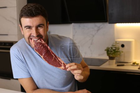 Foto de Retrato de un joven guapo sosteniendo carne cruda en la cocina - Imagen libre de derechos