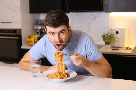 Foto de Retrato de un joven guapo comiendo espaguetis en la cocina - Imagen libre de derechos