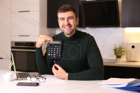 Téléchargez les photos : Portrait de beau jeune homme travaillant de la maison avec ordinateur portable à la cuisine - en image libre de droit