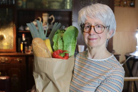 Foto de Close-up portrait of mature woman with paper bag of groceries at home - Imagen libre de derechos