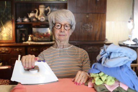 Foto de Close-up portrait of mature woman ironing clothes at home - Imagen libre de derechos