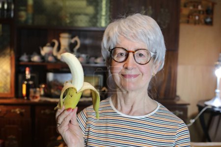 Foto de Close-up portrait of mature woman with banana at home - Imagen libre de derechos