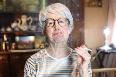 Foto de Close-up portrait of mature woman with cigarette smoking at home - Imagen libre de derechos
