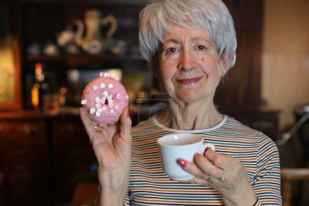 Photo for Close-up portrait of mature woman with doughnut and cup of coffee at home - Royalty Free Image