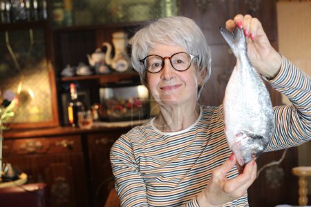Foto de Close-up portrait of mature woman with raw fish at home - Imagen libre de derechos