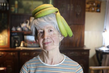 Foto de Close-up portrait of mature woman with branch of bananas at home - Imagen libre de derechos