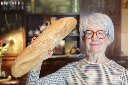 Foto de Close-up portrait of mature woman with freshly baked bread at home - Imagen libre de derechos
