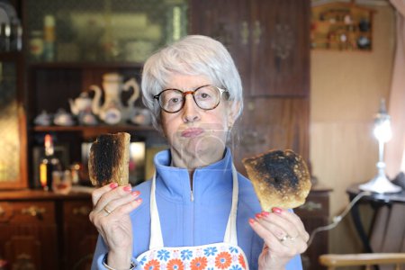 Foto de Close-up portrait of mature woman with overroasted toasts at home - Imagen libre de derechos