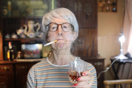 Téléchargez les photos : Close-up portrait of mature woman with cigarette and glass of whiskey at home - en image libre de droit