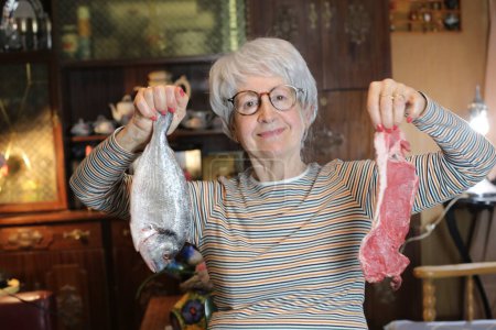 Photo for Close-up portrait of mature woman with raw fish and beef steak at home - Royalty Free Image