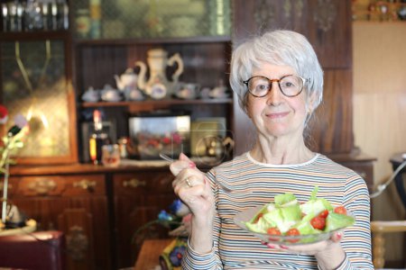 Photo for Close-up portrait of mature woman with bowl of salad at home - Royalty Free Image