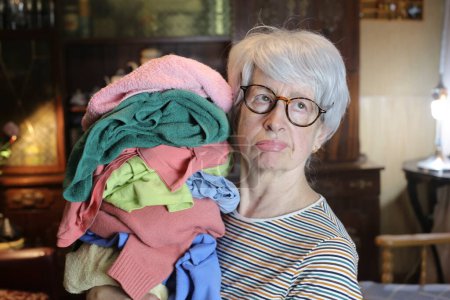 Foto de Close-up portrait of mature woman with stack of clothes at home - Imagen libre de derechos