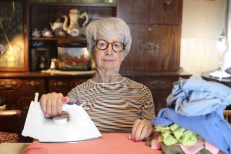 Foto de Close-up portrait of mature woman ironing clothes at home - Imagen libre de derechos