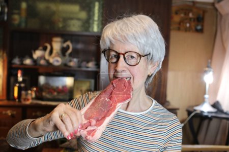 Téléchargez les photos : Close-up portrait of mature woman with raw beef steak at home - en image libre de droit