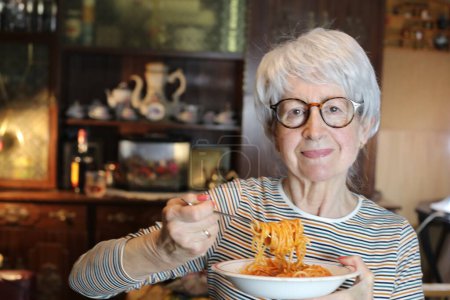 Photo for Close-up portrait of mature woman with plate of spaghetti at home - Royalty Free Image