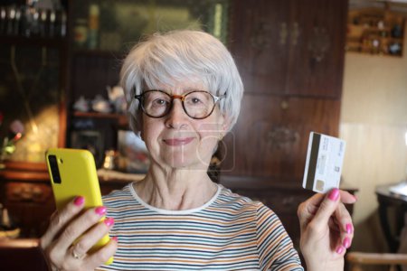Foto de Close-up portrait of mature woman with smartphone and credit card at home - Imagen libre de derechos