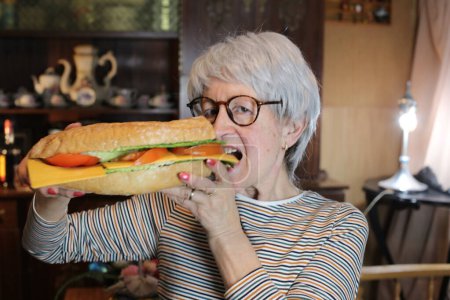 Photo for Close-up portrait of mature woman with giant sandwich at home - Royalty Free Image