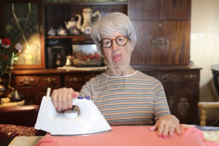 Téléchargez les photos : Close-up portrait of mature woman ironing clothes at home - en image libre de droit