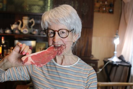 Photo for Close-up portrait of mature woman with raw beef steak at home - Royalty Free Image