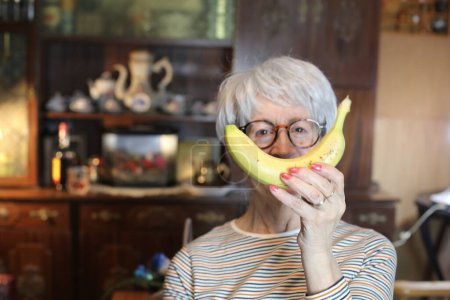 Foto de Close-up portrait of mature woman with banana at home - Imagen libre de derechos