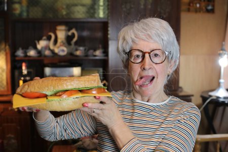 Foto de Close-up portrait of mature woman with giant sandwich at home - Imagen libre de derechos