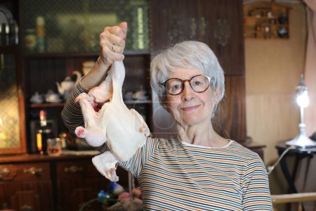 Photo for Close-up portrait of mature woman with raw chicken at home - Royalty Free Image