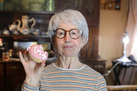 Foto de Close-up portrait of mature woman with glazed doughnut at home - Imagen libre de derechos