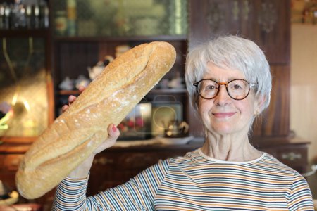 Foto de Close-up portrait of mature woman with freshly baked bread at home - Imagen libre de derechos