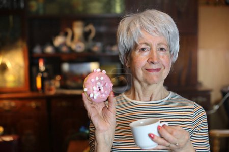 Photo for Close-up portrait of mature woman with glazed doughnut at home - Royalty Free Image