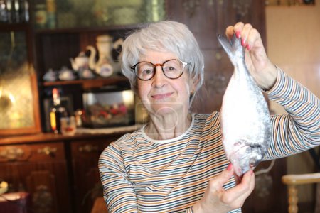 Foto de Close-up portrait of mature woman with raw fish at home - Imagen libre de derechos