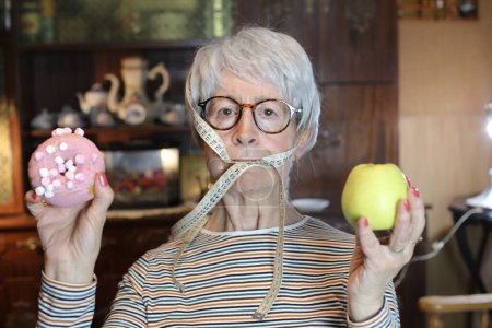 Téléchargez les photos : Close-up portrait of mature woman with glazed doughnut and green apple at home - en image libre de droit