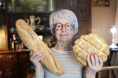 Photo for Close-up portrait of mature woman with freshly baked bread at home - Royalty Free Image