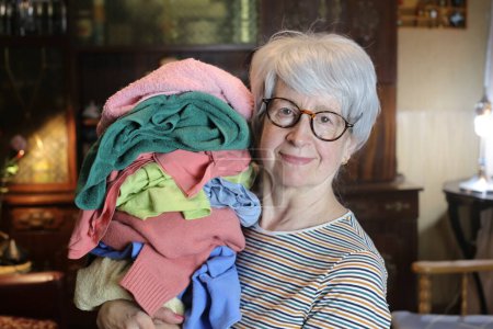 Photo for Close-up portrait of mature woman with stack of clothes at home - Royalty Free Image