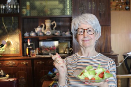 Photo for Close-up portrait of mature woman with bowl of salad at home - Royalty Free Image