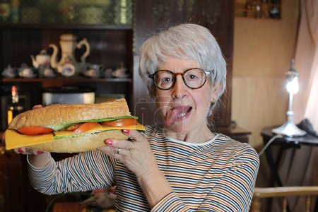Foto de Close-up portrait of mature woman with giant sandwich at home - Imagen libre de derechos