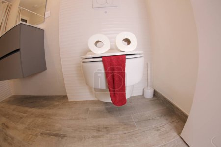 Téléchargez les photos : Wide angle shot of toilet with face made of paper rolls and red towel, comedy concept - en image libre de droit