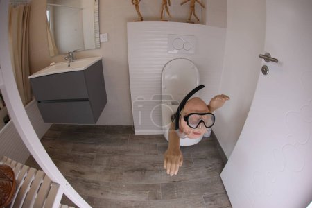 Photo for Wide angle shot of person with snorkel and diving mask sticking out of toilet, comedy concept - Royalty Free Image