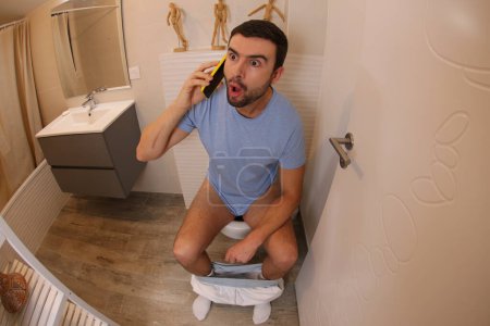 Téléchargez les photos : Plan grand angle de jeune homme exprimé parlant par téléphone dans les toilettes - en image libre de droit