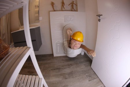 Téléchargez les photos : Wide angle shot of person with hard hat sticking out of toilet, comedy concept - en image libre de droit