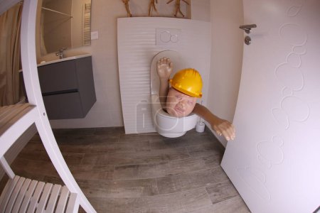 Téléchargez les photos : Wide angle shot of person with hard hat sticking out of toilet, comedy concept - en image libre de droit