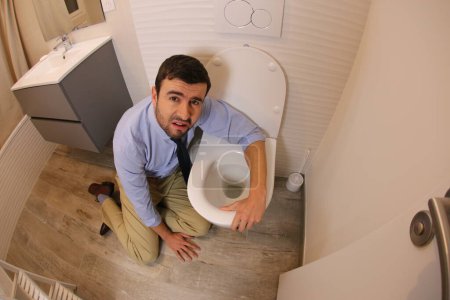 Téléchargez les photos : Wide angle shot of young man vomiting in toilet - en image libre de droit