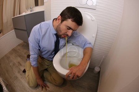 Téléchargez les photos : Wide angle shot of young man vomiting in toilet - en image libre de droit