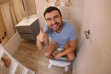 Téléchargez les photos : Wide angle shot of young man in toilet showing thumb up - en image libre de droit