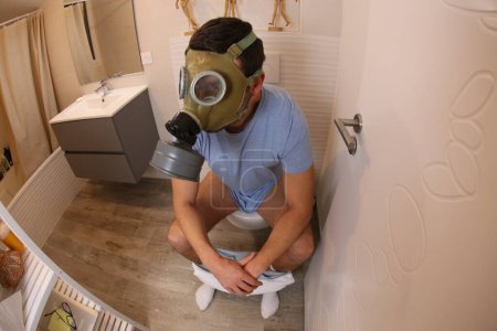 Téléchargez les photos : Wide angle shot of young man with gas mask in toilet - en image libre de droit