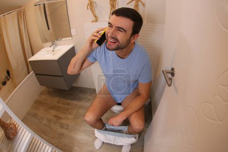 Téléchargez les photos : Wide angle shot of expressed young man talking by phone in toilet - en image libre de droit