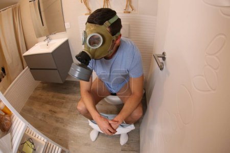 Téléchargez les photos : Plan grand angle de jeune homme avec masque à gaz dans les toilettes - en image libre de droit